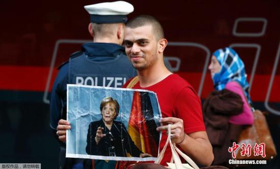 当地时间9月5日，德国慕尼黑，成千上万的移民途径匈牙利和奥地利抵达德国，来自叙利亚的难民手举德国总理默克尔的照片。德国总理默克尔此前表示，可以在不增税和影响预算的情况下应付新抵达的难民潮。