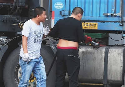 9月25日，天津滨海泰达大街北侧临近京津塘高速入口。一名黑衣男子正在给一辆大货车加油，一名男子在一旁抽烟。