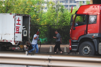 9月25日，在天津滨海泰达大街北侧，临近京津塘高速入口处。一男子正拿着加油枪去给大货车加油。而他的加油车是左边改装的小厢式货车。A10-A11版摄影/新京报记者 大路