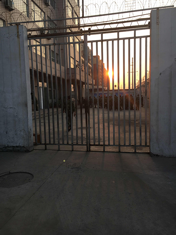 济南科技防卫专修学院的学生在公寓楼下站队打饭，四处都是铁栅栏和铁丝网。